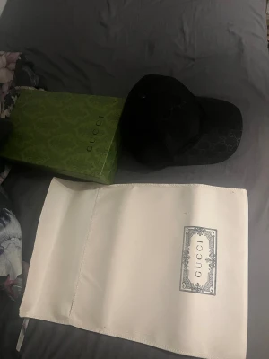 Svart Gucci keps med GG-mönster - Säljer en svart Gucci keps med klassiskt GG-monogram över hela framsidan. Kepsen har mesh på baksidan och justerbar snapback. Materialet är en mix av polyester och syntet, vilket gör den lätt och bekväm. Medföljer originalkartong och dustbag, storlek M .