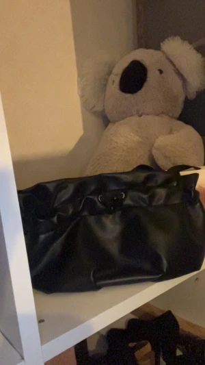 Svart handväska i skinnimitation - Snygg svart väska i skinnimitation med mjuk, slät yta och praktisk snörning upptill. Väskan har en enkel och stilren design som passar till många olika outfits. Perfekt storlek för att få plats med allt du behöver under dagen. Man kan bära väskan i handen men den har även ett längre band så att man kan ha den på axeln. Från ( byCarinWester)