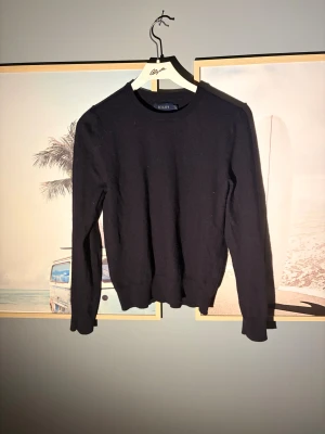 Svart kashmirtröja från Riley - Svart kashmirtröja från Riley med rund hals och lång ärm. Tröjan har en clean och klassisk look med ribbade muddar vid ärmslut och nederkant. Perfekt för dig som gillar stilrena och mjuka plagg.