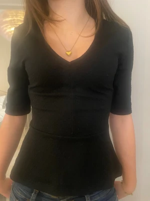 Svart v-ringad blus med trekvartsärm - Snygg svart blus med v-ringning och trekvartsärmar. Modellen är figurnära upptill och har en lätt utsvängd nederdel som ger en cool siluett. Materialet är strukturerat och känns mjukt mot huden. Perfekt att styla med jeans eller kjol för en trendig look. Skriv för fler bilder och mått💞