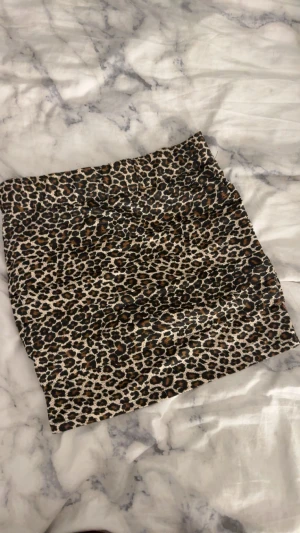 Leopardmönstrad kortkjol - Snygg kortkjol med leopardmönster i svart, beige och bruna toner. Kjolen har en tight passform och är perfekt för dig som vill sticka ut med en trendig look. Materialet känns mjukt och följsamt mot kroppen.