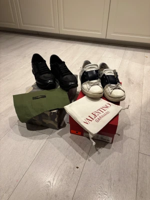 Valentino Rockrunner & Garavani sneakers säljs ihop - Två par Valentino sneakers säljes! Ett par svarta Rockrunner med stl 42 camouflagemönster, snörning och detaljer i skinn och mocka. Det andra paret är vita Garavani open stl 41  . Båda kommer med originalkartong och dustbag. Obs. Dem vita valentino open är skadade och har släppt sulan där fram. Men med lite sko färg och lim kan du få dem rätt schyssta igen. Rockrunnerserna är in princip nya använt 10-12 gånger på sin höjd. Priset kan diskuteras vid snabb affär 