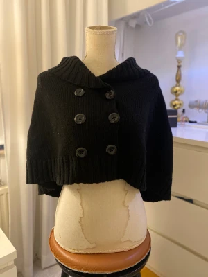 Svart poncho - Super gullig svart poncho  med stora knappar och elegant form. I uppskattad storlek är den S-M men väldig flexibel även för storlek XS-L.  I bra skick men använt! Inga defekter så långt jag kan se. Skriv kring bilder och frågor❤️
