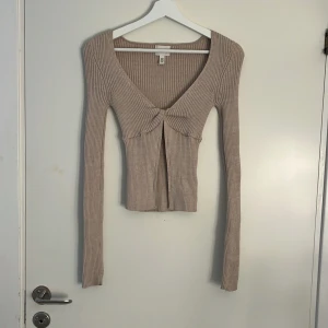 Beige ribbad croppad topp H&M - ‼️LÄS MIN BIO ‼️Säljer en beige ribbad croppad topp från H&M med lång ärm och snygg v-ringning. Toppen har twistad detalj framtill och är figurnära i modellen. Perfekt att styla med jeans eller kjol för en trendig look.