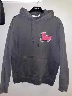 Mörkgrå hoodie med rosa patch - Säljer en mörkgrå hoodie från Weekday med en ficka framtill och snörning vid huvan. På bröstet sitter en cool rosa patch som ger tröjan en unik vibe. Den passar lite boxigt och är perfekt för dig som gillar streetwear och vill sticka ut lite extra. Skriv vid intresse!