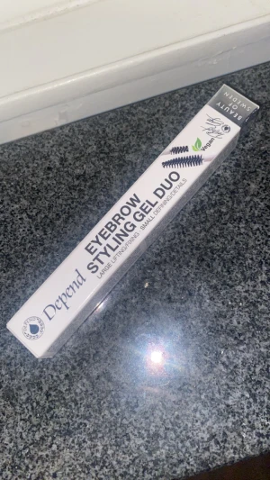 Depend Eyebrow Styling Gel Duo - Eyebrow Styling Gel Duo från Depend med två borstar, en stor för lyft och fixering och en liten för detaljer. Transparent gel som ger snygg form och stadga till brynen. Vegansk formula i vit förpackning med svart text.