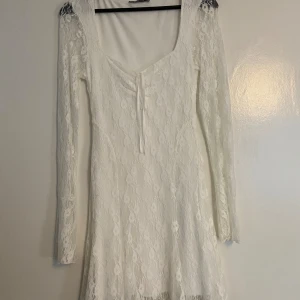 Vit spetsklänning från Gina Tricot - Superfin vit kort spetsklänning från Gina Tricot med långa ärmar och v-ringning med knyt framtill. Klänningen har figurnära passform och är helfodrad under spetsen. Perfekt för midsommar, studenten eller som en sommar klänning. I storlek M men passar som S. köpt för 600 kr och använd 1 gång.