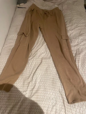 Beige cargopants med snörning, strl M - Säljer ett par beige cargopants från 157 i storlek M. Byxorna har mjukt material, elastisk midja med snörning och stora fickor på sidorna. Perfekt för chill dagar och streetwear-stil.