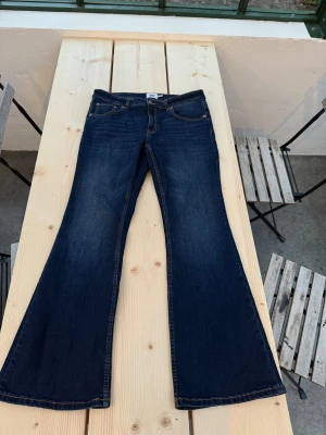 Mörkblå bootcut jeans från 157 - Mörkblå jeans från 157 med klassisk femficksdesign och snygg bootcut-passform. Jeansen har kontrastsömmar och är tillverkade i ett stretchigt denimtyg som sitter skönt. Perfekta för dig som gillar en retroinspirerad look med utsvängda ben.