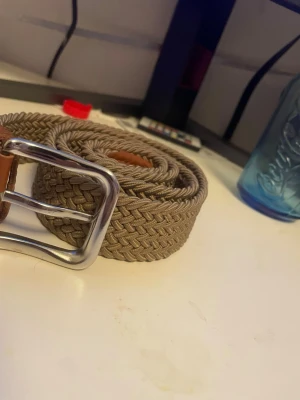 Beige flätad bälte från Jack & Jones - Säljer ett snyggt beige flätat bälte från Jack & Jones med detaljer i brunt skinn och ett silvrigt metallspänne. Perfekt accessoar för att lyfta din outfit och funkar till både jeans och chinos.