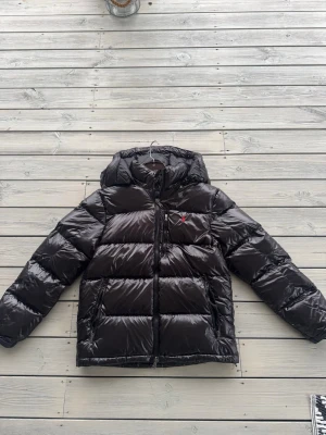 Svart pufferjacka från Polo Ralph Lauren - Säljer en svart pufferjacka från Polo Ralph Lauren med blank finish och röd logga på bröstet. Den är bara provad. Kommer puffa ut mer vid användning då den bara hängt tillsammans med andra jackor. Storlek L men passar åt M hållet. Har även en till likadan i M som passar S.