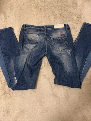 Blå distressed jeans från ONLY - Säljer ett par blå jeans från ONLY med slitna detaljer och snyggt tvättad look. Jeansen har fem fickor, normal passform och klassisk midja. Materialet är jeans i bomull och de har en rak siluett med slitningar på benen för en trendig vibe.