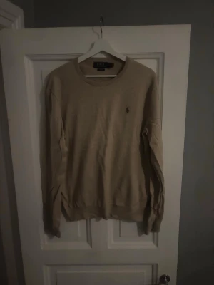 Beige tröja från Polo Ralph Lauren - Snygg beige tröja från Polo Ralph Lauren i slim fit-modell. Klassisk rund halsringning och diskret logga broderad på bröstet. Tillverkad i mjuk bomull och har långa ärmar. Perfekt för dig som gillar stilrena och tidlösa plagg. Knappt använd, ligger bara och tar plats, köpt i sommras. 