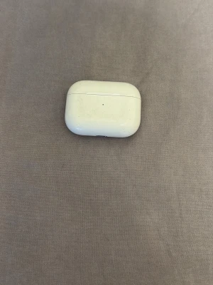 AirPods Pro - Apple AirPods Pro med laddningsetui. Etuiet har tydliga tecken på användning med repor och smuts, men är fullt funktionellt. Perfekt för dig som vill ha trådlösa hörlurar med aktiv brusreducering och hög ljudkvalitet till ett bra pris.