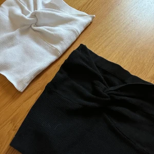 Svart och vit ribbad bandeau tubtopp - Två bandeau tubtoppar i svart och vitt, båda i ribbat material med snygg twistad knut framtill. Perfekta att styla med höga jeans eller kjol för en clean look. Toppens stretchiga tyg gör den bekväm och sitter på plats hela dagen. 