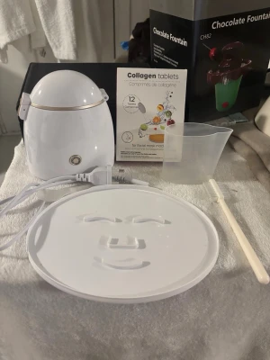 Maskin för ansiktsmask med kollagentabletter - Säljer en vit ansiktsmaskmaskin med tillbehör som mätskopp, borste och kollagentabletter. Maskinen blandar ingredienser till en ansiktsmask som formas på den medföljande maskbrickan. Perfekt för dig som vill göra egna sheet masks hemma. Den är gul inuti pga att jag använde den med gurkmeja och har diskat den 3 gånger men det går tyvärr inte bort. 