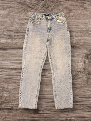 Högmidjade ljusa jeans från Vero Moda - Snygga högmidjade jeans från Vero Moda i en ljusblå tvätt med raka ben och klassiska fem fickor. Jeansen har en vintagekänsla med slitna detaljer och guldfärgade sömmar. Perfekta för en chill och trendig look.