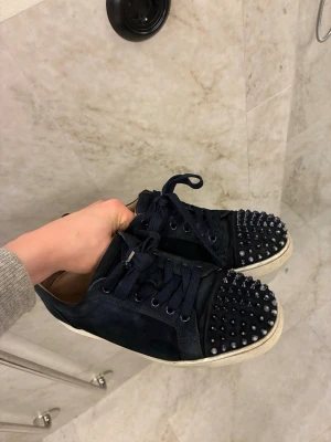 Louboutin skor - Säljer ett par mörkblå sneakers i mocka från Christian Louboutin med ikoniska röda sulor. Skicket är bra och storleken är 41/42 Inga defekter bara små tecken på användning. Hör av er vid frågor!