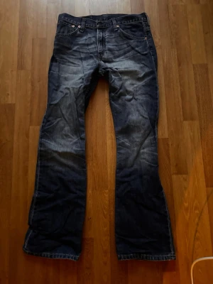 Levis 517 blå bootcut jeans - Säljer ett par klassiska Levis 517 jeans i mörkblå tvätt med bootcut passform. Jeansen har fem fickor, dragkedjegylf och snygga slitningar framtill. Perfekta för dig som gillar retrovibbar och tidlös denimstil.
