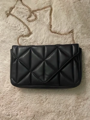 Svart quiltad axelväska med kedja - Säljer en svart quiltad axelväska med guldfärgad kedjerem🖤 från h&m