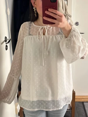 Blus från Vila - Vacker, vit blus med knytdetalj och spetsdetaljer. Den är gjord av ett lätt och luftigt tyg. Storlek S💕