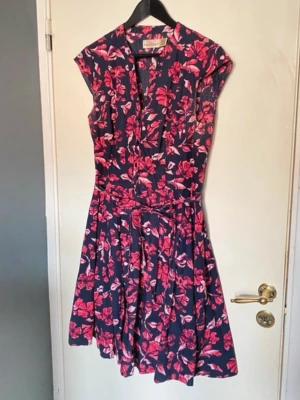 Klänning med knappar / dress with buttons / sukienka zapinana na guziki - En fin klänning i svart och fler nyanser av rosa blommor. Klänningen har en krage. Det är svårt att se på bilderna men klänningen har endast knappar från ca 10 cm ner från kragen till hela vägen ner. Med kommer även ett band man kan knyta runt midjan (se bilderna). Tyget är luftigt.  Material: 100% bomull