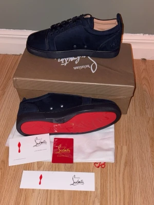 Blå mocka sneakers från Christian Louboutin - Säljer ett par riktigt snygga blå sneakers från Christian Louboutin i mocka med den ikoniska röda sulan. Skorna har snörning, rund tå och diskret broderad logga på hälen. Insidan är i beige läder och sulan är i rött gummi med signaturdetalj.