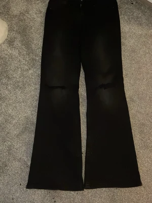 Svarta bootcut jeans från ONLY - Säljer ett par svarta bootcut jeans från ONLY med slitningar vid knäna. Jeansen har klassisk femficksdesign, låg midja och är tillverkade i stretchig bomullsblandning för skön passform. Perfekta för dig som gillar en trendig och avslappnad look.