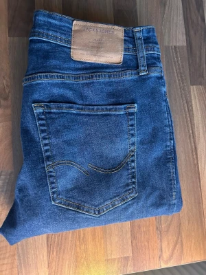 Blå slim jeans från Jack & Jones - Snygga blå jeans från Jack & Jones i modellen Slim/Glenn. Klassisk femficksdesign med kontrastsömmar och läderpatch bak i midjan. Jeansen har en slim passform och är tillverkade i mjukt denimtyg som sitter skönt hela dagen.