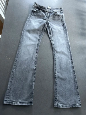 Grå lågmidjade utsvängda jeans från Gina Tricot 164 - Sparsamt använda i fint skick. Inga fläckar eller hål. Lite skrynkligt i tyget på ena låret (har inte sett det vid användning). Storlek 164, passar XS. Tvättar utan sköljmedel och torktumlar inte kläder.