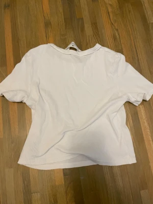 Vit ribbad t-shirt från H&M - Enkel och stilren vit t-shirt från H&M i ribbad bomull. Modellen har korta ärmar och en något boxig passform som ger en avslappnad vibe. Perfekt att matcha med jeans eller kjol för en clean look.