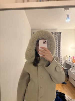 Beige ulljacka med fuskpälsluva - Säljer en beige jacka från Gina Tricot med stor fluffig luva i fuskpäls. Perfekt för kalla dagar när du vill vara både varm och snygg.jackan är helt ny har använd den två gånger säljer den pågrund av att jag inte använder den