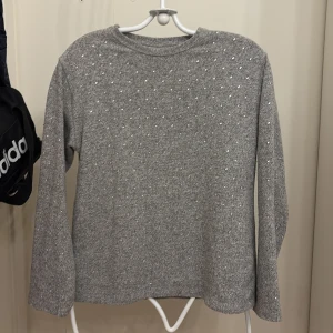 Grå stickad tröja med pärlor - Mysig grå stickad tröja dekorerad med små pärlor över hela framsidan och ärmarna. Tröjan har rund halsringning och långa ärmar, perfekt för kyligare dagar. Enkel men ändå lite extra tack vare pärldetaljerna. Storlek 152 men skulle säga den passar som XS då den är lite oversized!!