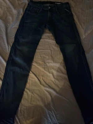 Blå Replay jeans  - Säljer ett par klassiska blå jeans från Replay med raka ben och snygga detaljer på bakfickorna. Jeansen har normal passform och är tillverkade i slitstarkt denimtyg. Perfekta för dig som gillar en enkel och tidlös look.