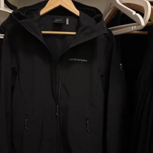Peak Performance Explore M Jacka. - Säljer en svart vindjacka från Peak Performance jag köpte för 1 vecka sedan. Stilren och helt ny med huva och dragkedja framtill. Nypris 2199kr. Perfekt för dig som vill ha en stilren och clean look.  
