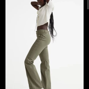 Olivgröna bootcut cargopants - Snygga olivgröna cargopants med bootcut-snitt och låg midja. Byxorna har coola fickor med lock och knapp framtill samt markerade sömmar längs benen. Tillverkade i ett mjukt bomullsmaterial med lite stretch för skön passform. Knappt använda