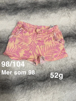 Rosa blommiga shorts med volang - Säljer ett par shorts med blommönster och blad, elastisk midja och volangdetaljer vid fickorna. Perfekta för varma dagar och riktigt sköna att ha på sig.🌸 Fint använt skick. Storlek 98/104 men upplever mer som 98