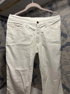 Vita raka jeansbyxor med broderade fickor - Säljer ett par vita jeansbyxor med raka ben och snygga broderade detaljer på bakfickorna. Klassisk femficksmodell med bälteshällor. Perfekta till en clean och fräsch look. Materialet känns mjukt och skönt mot huden.