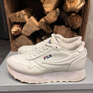 Vita Fila Orbit Zeppa sneakers - Säljer ett par vita Fila Orbit Zeppa sneakers med plattformssula och klassisk Fila-logga i blått och rött på sidan, hälen och tungan.. Perfekta för dig som gillar chunky sneakers med retrovibe.