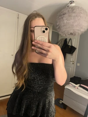 Glittrig svart tubtopp Sisters Point - Säljer en glittrig svart tubtopp från Sisters Point i storlek M. Toppen är axelbandslös och har en volang nertill som ger en snygg siluett. Perfekt för dig som vill sticka ut med lite extra glitter. Materialet är stretchigt och bekvämt.