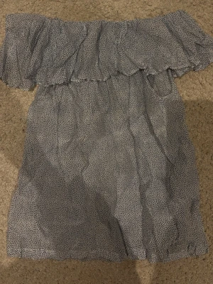 offshoulder prickig topp - Säljer en söt offshoulder topp i vitt med små blåa prickar. Toppen har volang runt axlarna och är ärmlös, vilket ger en luftig och somrig känsla. 