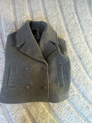 Snyggaste kappan!  - Säljer en grå kort kappa från lager 157 i storlek XS. Jackan har bred krage, dubbelknäppning med stora knappar. Säljer eftersom att den inte används. Två av knapparna har trillat av men de är påsydda igen. Nypris : 400 