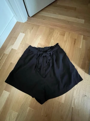 Svarta shorts med knyt i midjan - Ett par svarta kostymshorts från H&M med ett knytband i midjan. Storlek 44, L