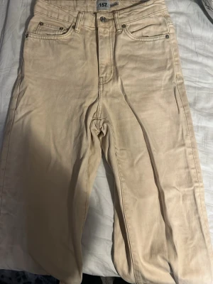 Beiga jeans från 157 i XS - Snygga beiga jeansbyxor från 157 i storlek XS. Klassisk femficksmodell med raka ben och normal passform. Byxorna är tillverkade i bomull och har bälteshällor samt knapp- och dragkedjestängning. Perfekta för en chill och stilren look.