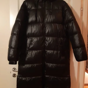 Svart lång dunjackaLång jacka M - endast provad, oanvänd. - Säljer en svart lång dunjacka i mycket bra skick. Perfekt för kalla vinterdagar med sin varma och puffiga design. Jackan har långa ärmar och en praktisk huva för extra skydd mot kyla. Den är stilren och passar till de flesta outfits. Perfekt för vinterns alla äventyr! 🖤
