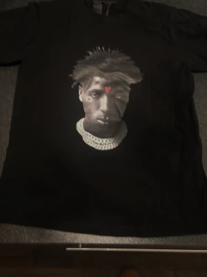 Svart VLONE t-shirt med tryck - Svart t-shirt från VLONE med stort rött V-tryck på ryggen och ett grafiskt tryck framtill. Klassisk passform och korta ärmar, tillverkad i mjuk bomull. Perfekt för dig som gillar streetwear och vill sticka ut med en ikonisk design.