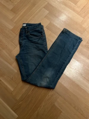 Levis 511 blå jeans tapared fit - Klassiska Levis 511 jeans i blå tvätt med raka ben och normal passform. Jeansen har fem fickor, knappgylf och den ikoniska Levis-lappen bak i midjan. Tillverkade i slitstarkt denim med snyggt slitna detaljer för en avslappnad look.  Storlek 14A ca 165cm