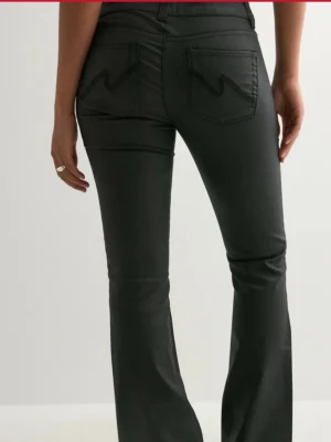 Svarta bootcut byxor från Nelly (low waist) - Snygga svarta byxor med bootcut passform och hög midja. Byxorna har fram- och bakfickor, dubbla knappar i midjan och markerade sömmar längs benen. Materialet har en lätt glansig finish som ger en modern look. Aldrig använda!!! För stora 