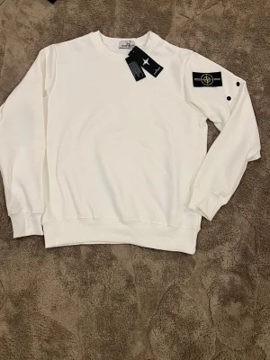 Vit sweatshirt från Island - Säljer en clean vit sweatshirt från  Island med klassisk logga på ärmen. Tröjan har rund hals, långa ärmar och ribbade muddar. Perfekt för dig som gillar stilrena och exklusiva plagg. Materialet är mjuk bomull.