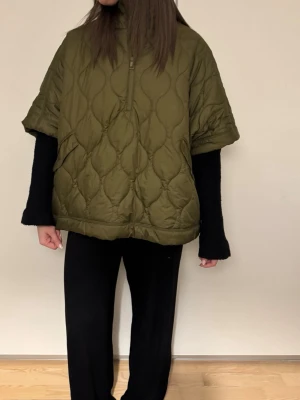 Olivgrön quiltad dunväst från H&M - Säljer en oversized olivgrön quiltad dunväst från H&M. Västen har hög krage, korta ärmar och en half zip-dragkedja framtill. Praktiska fickor med knappstängning och coolt mönstrad yta. Perfekt lager på lager-plagg för höst och vinter.